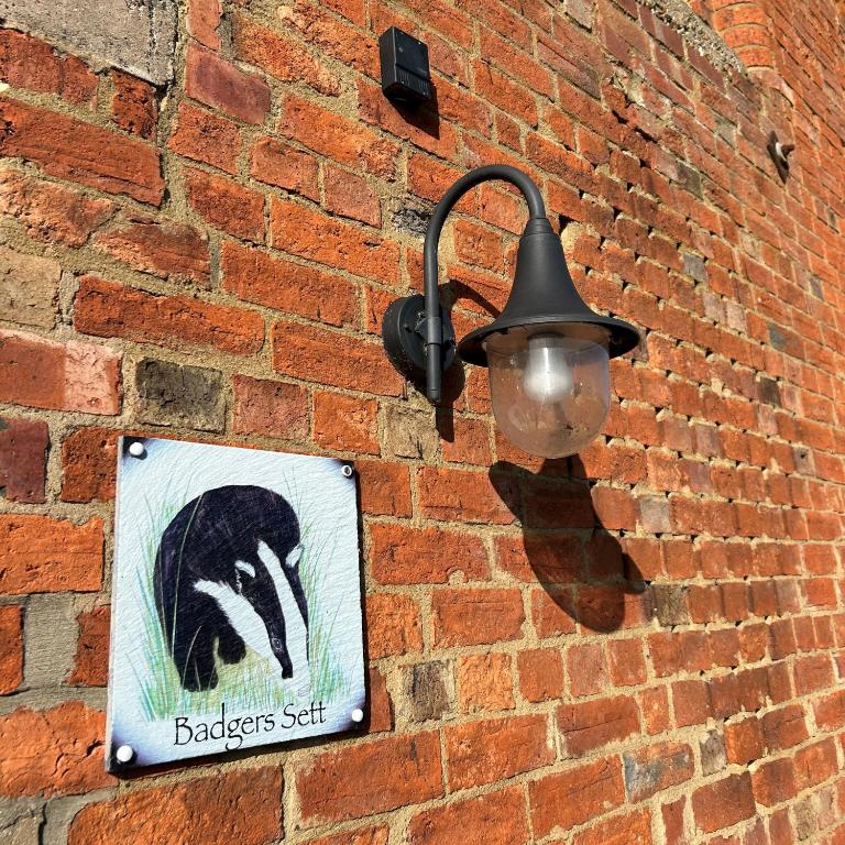 Una luz en una pared de ladrillo con un cartel. en Badgers Sett at Tove Valley Cottages, en Towcester