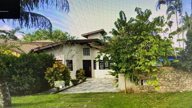 a white house with a stone wall and trees at Paraíso NA PRAIA - CASA 3 SUITES MAX 8 PESSOAS in Bertioga