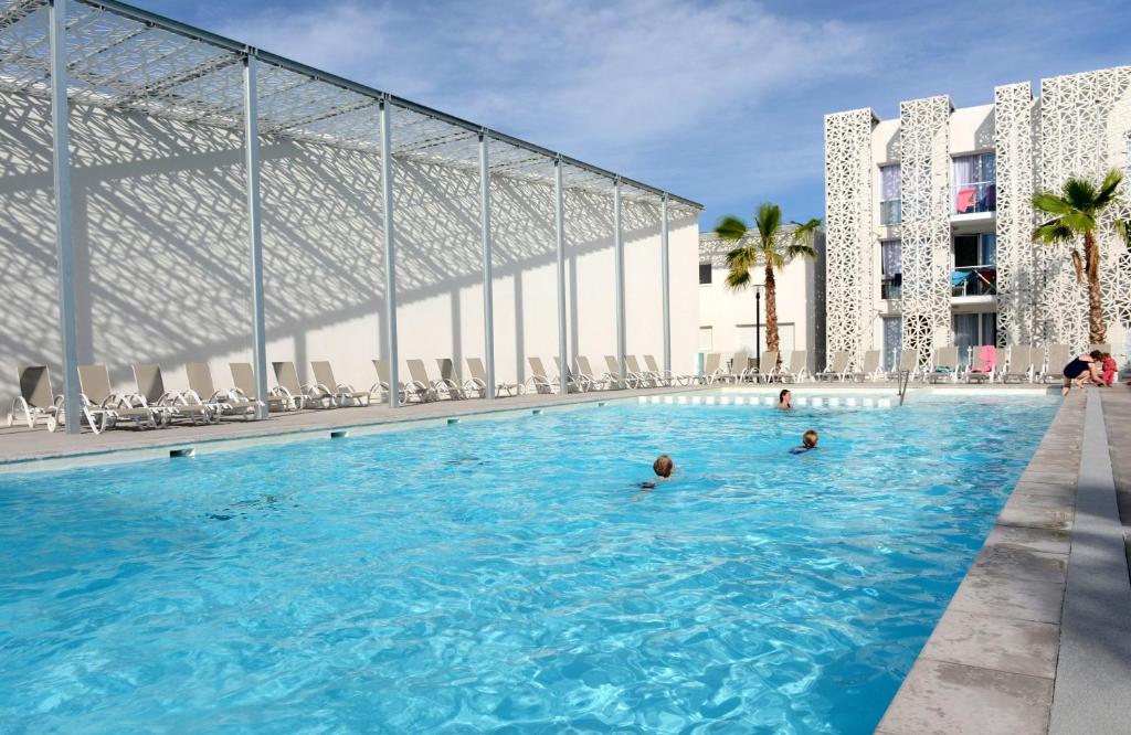 a swimming pool next to a building with palm trees at Résidence Prestige Odalys Nakâra in Cap d'Agde