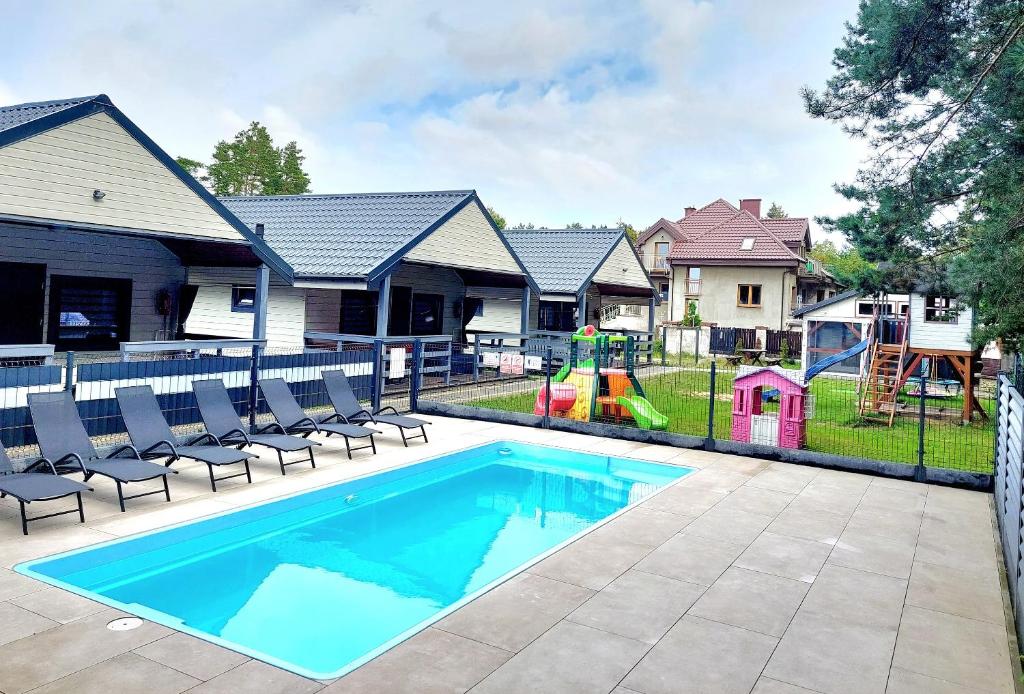 uma piscina com cadeiras e um parque infantil em Bursztynowo Domki Letniskowe em Ostrowo