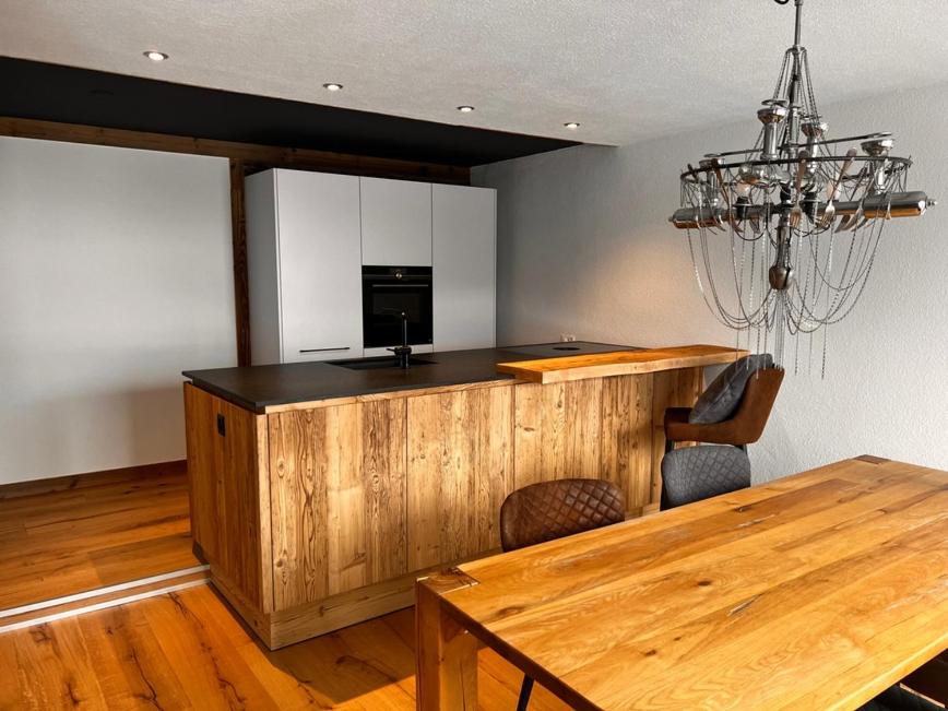 Il comprend une cuisine avec un comptoir en bois, une table et un lustre. dans l'établissement Mountaindream Apartment, à Sedrun