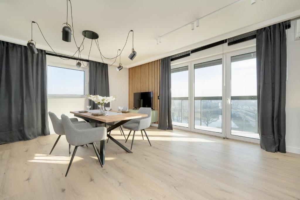 a dining room with a table and chairs and windows at Exclusive River View Apartment with Balcony & FREE GARAGE by Renters Prestige in Wrocław