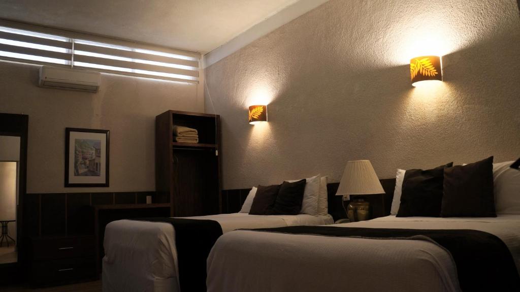 Fresnillo de González EcheverríaにあるHotel Casa Blancaのベッド2台、壁に照明が備わるホテルルームです。