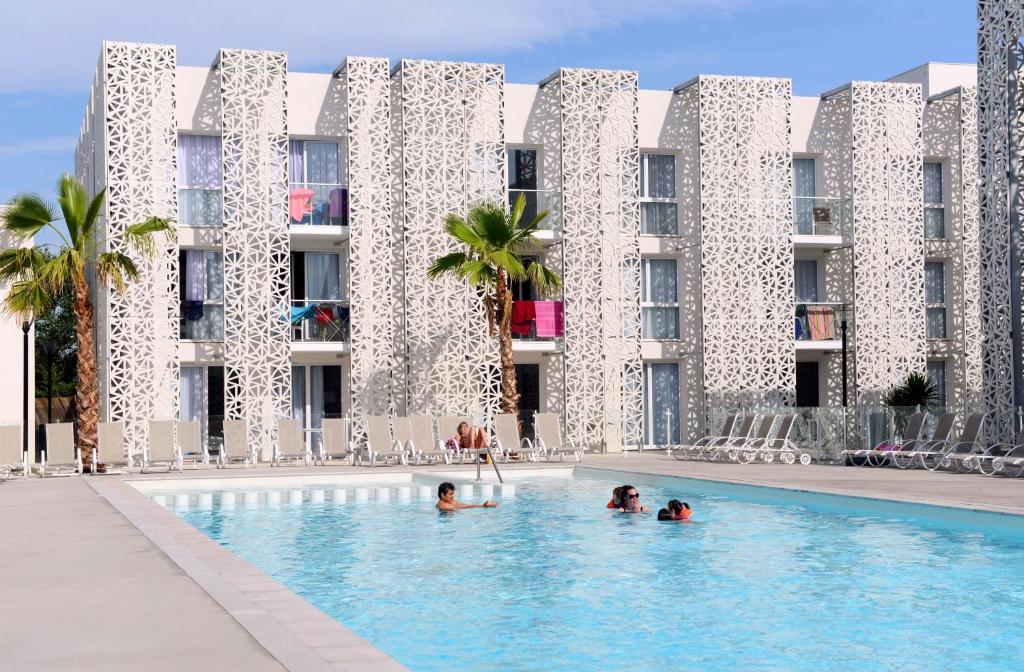 un groupe de personnes dans une piscine en face d'un bâtiment dans l'établissement Appart'Hotel Prestige Odalys Nakâra, au Cap d'Agde
