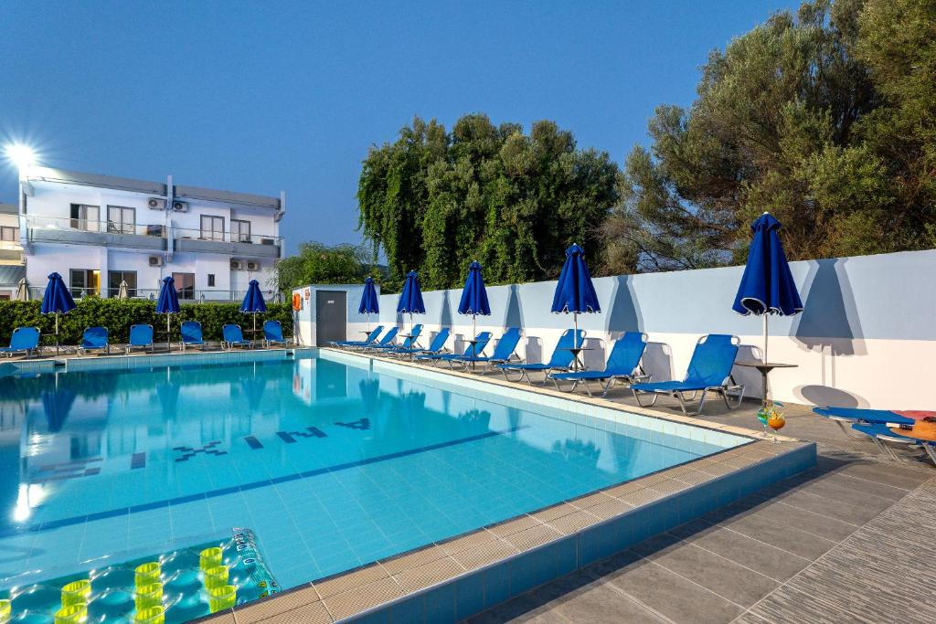 a swimming pool with chairs and blue umbrellas at Anixis Hotel & Apartments in Ialyssos