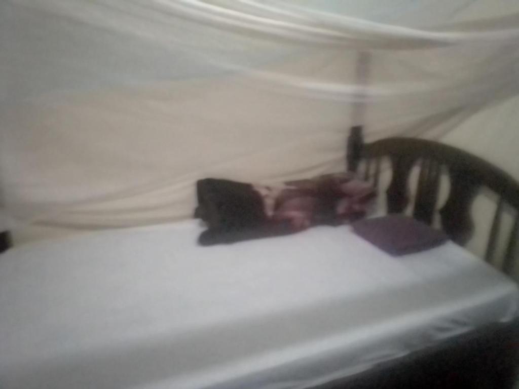 ein Kind, das auf einem Bett mit einem weißen Laken liegt in der Unterkunft Pilgrims home in Kampala