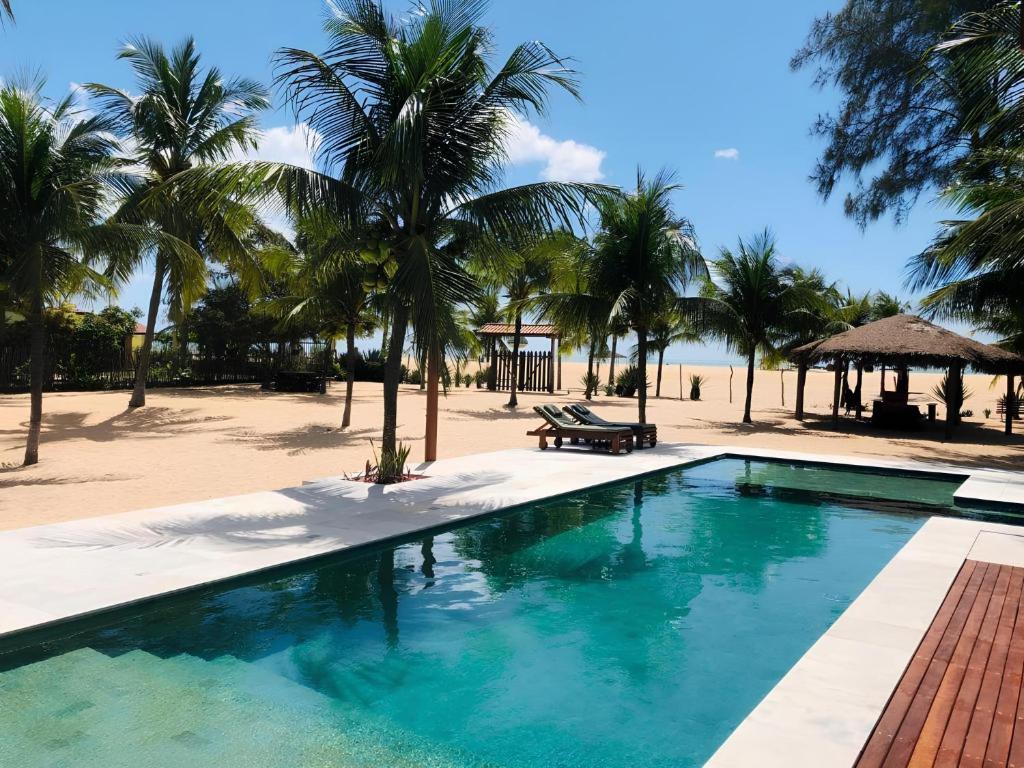 a swimming pool next to a beach with palm trees at Pousada Recanto da Praia in São Miguel do Gostoso