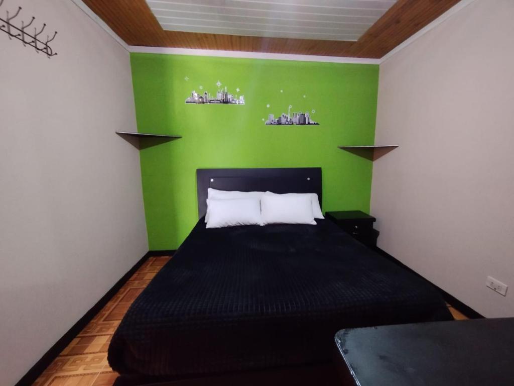 a green bedroom with a bed with a black bedspread at Habitaciones con baño privada Quiroga in Bogotá
