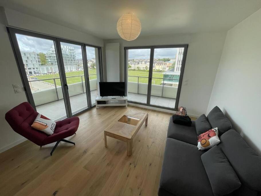 a living room with a couch and chairs and a tv at Presqu'île, appartement neuf avec balcon, salle de gym et parking in Caen