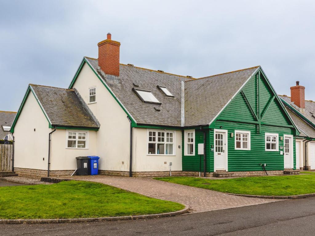 a green and white house with a driveway at Armstrong Cottages No30 in Bamburgh