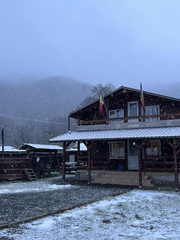 a snow covered house with flags on top of it at Cabană la poalele munților cu ciubăr in Jieţ