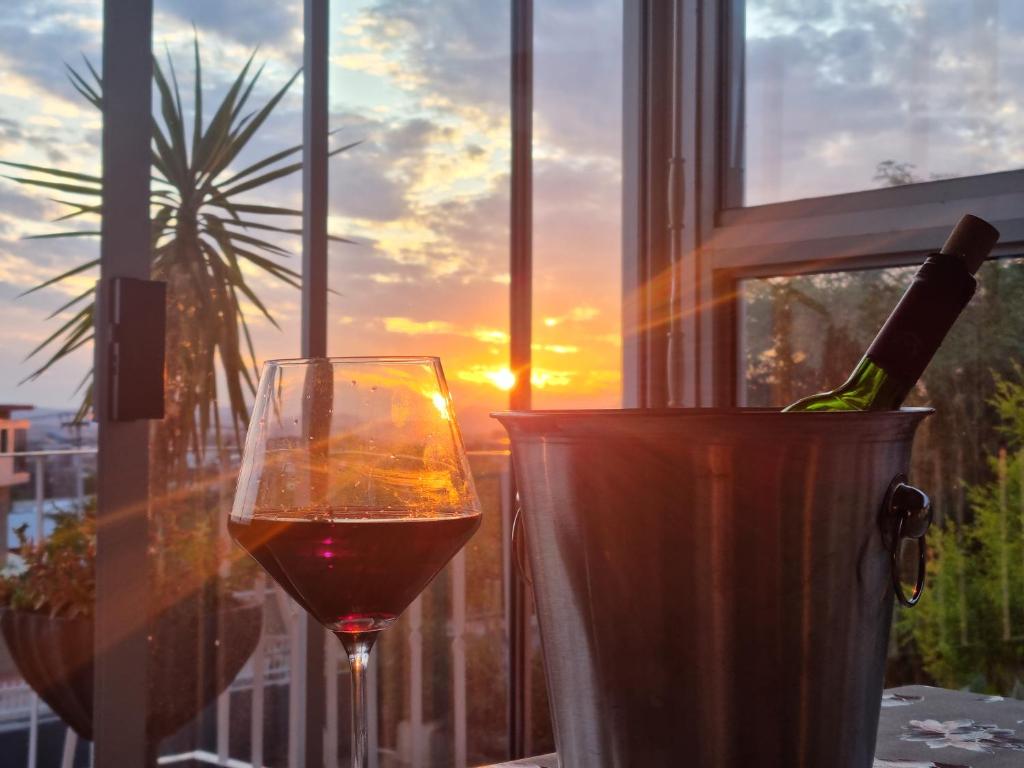 a glass of wine sitting next to a window with the sunset at SapphireA@54 in Windhoek