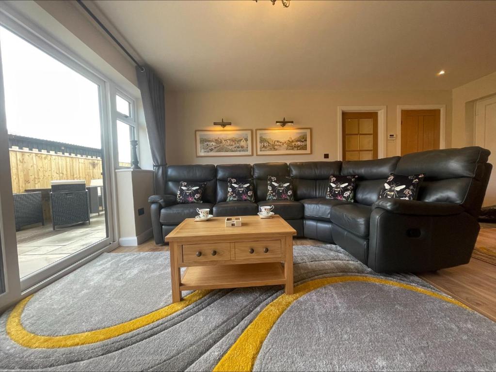 een woonkamer met een zwarte leren bank en een salontafel bij Bumblebee Barn, Luxury contemporary holiday home in Perranporth