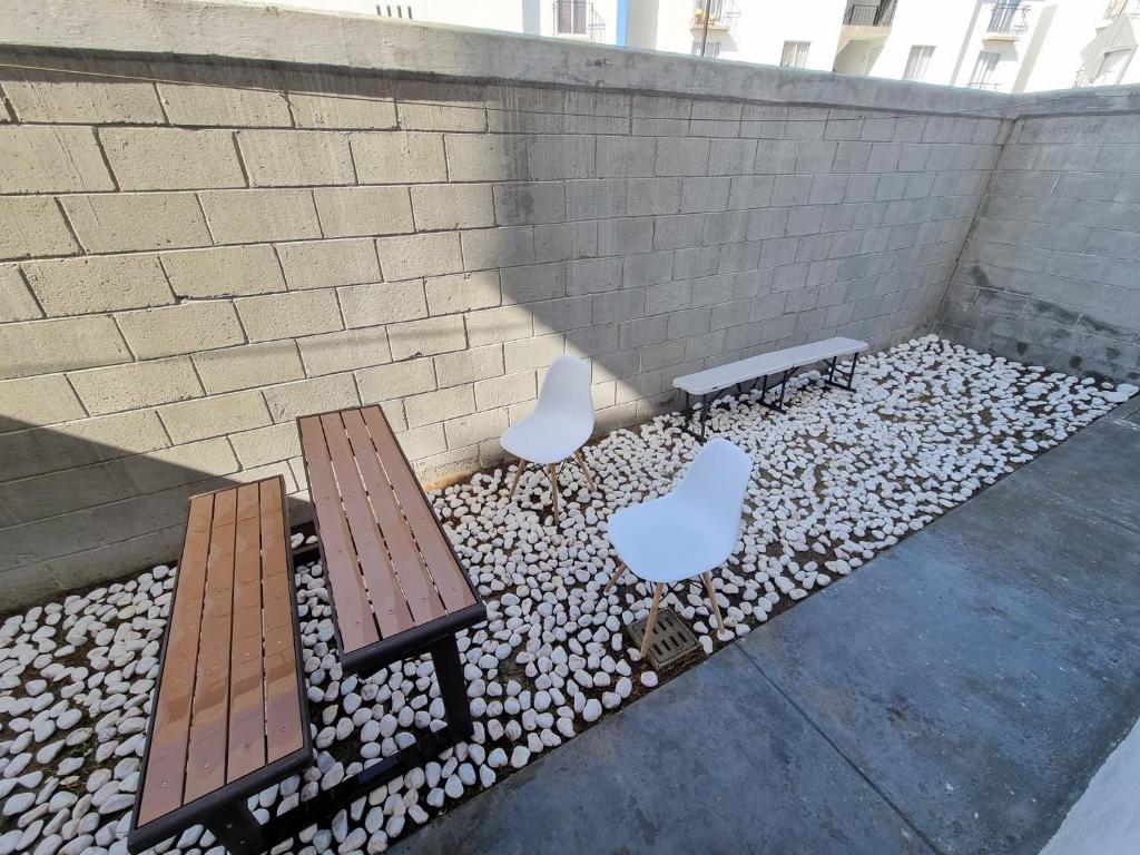 two benches and two white chairs in front of a brick wall at Depa muy ubicado Cortes 15B in Querétaro