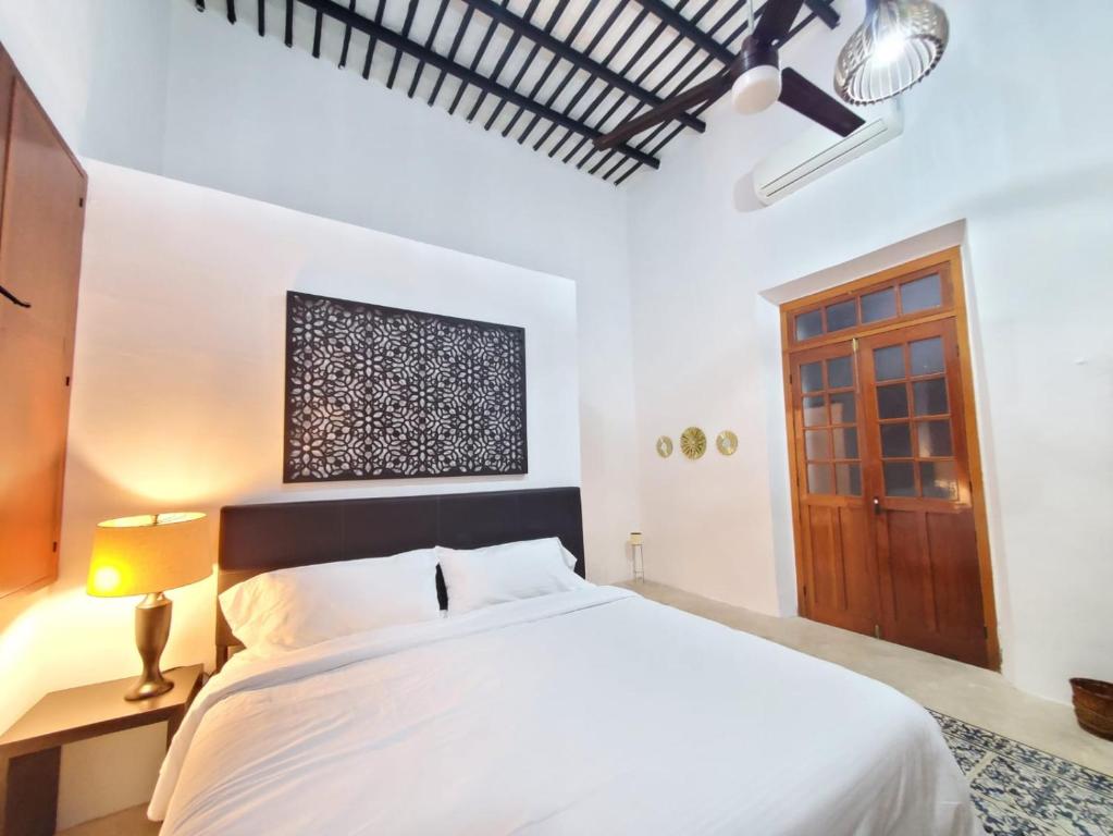 a bedroom with a white bed and a wooden door at CASA XTABENTUN in Mérida