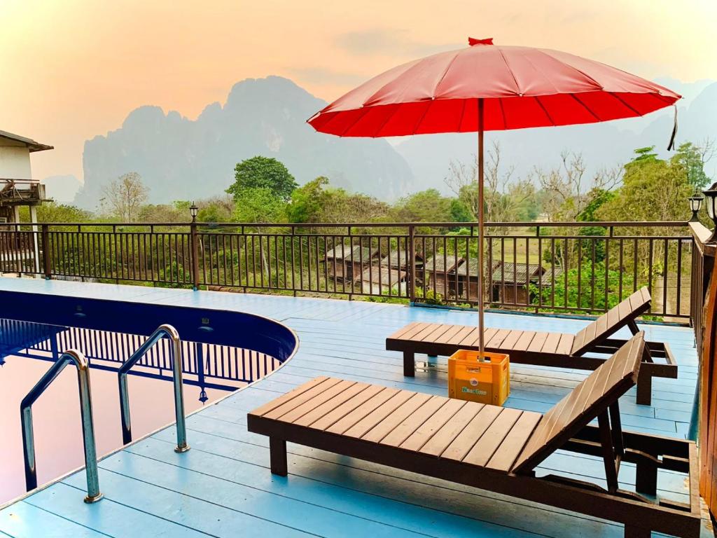 uma piscina com dois bancos e um guarda-sol vermelho em Happy Riverview Hotel em Vang Vieng