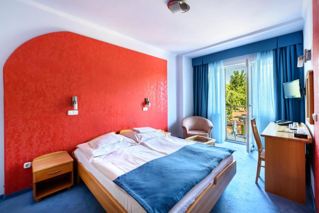 sypialnia z łóżkiem z czerwoną ścianą w obiekcie Hotel Négy Évszak w Hajduszoboszlo