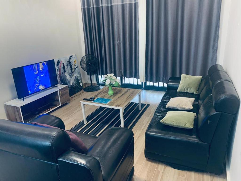 ein Wohnzimmer mit einem schwarzen Ledersofa und einem Tisch in der Unterkunft Exquisite Apartments- 1Bedroom Kigali in Kigali