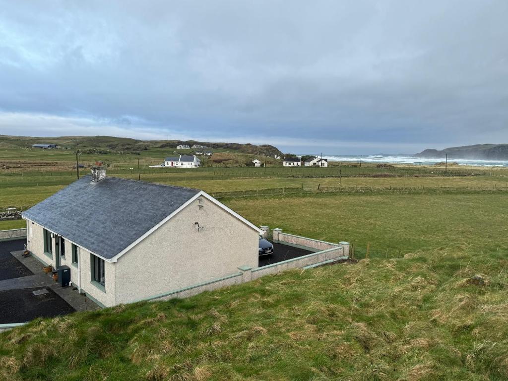 un edificio blanco en un campo junto al océano en Hughie's Farm Cottage, en Ballyliffin