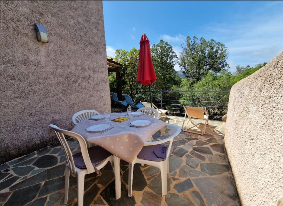 - une table avec des chaises et un parasol rouge sur la terrasse dans l'établissement Petit nid douillet à deux pas de Santa Giulia, à Porto-Vecchio