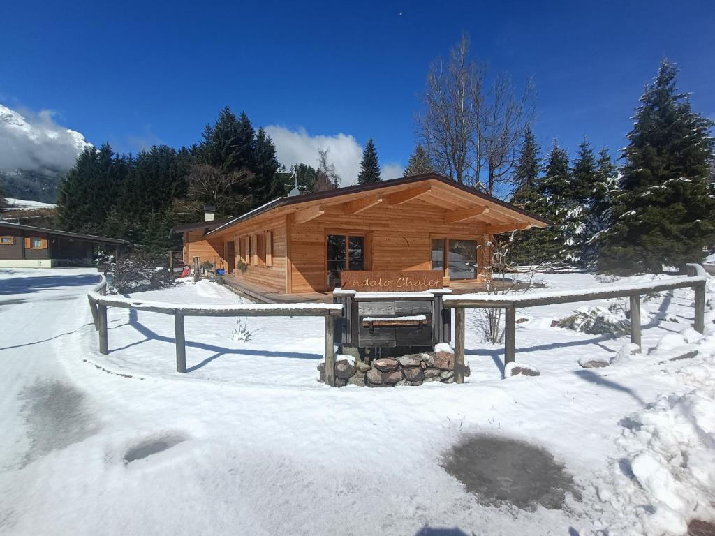 una cabaña de madera en la nieve con un molino de nieve delante en Andalo Chalet, en Andalo