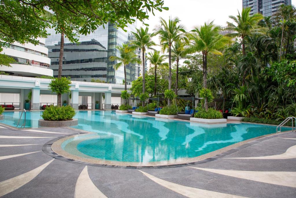 A curving outdoor pool surrounded by palms, planting and high-rise buildings.