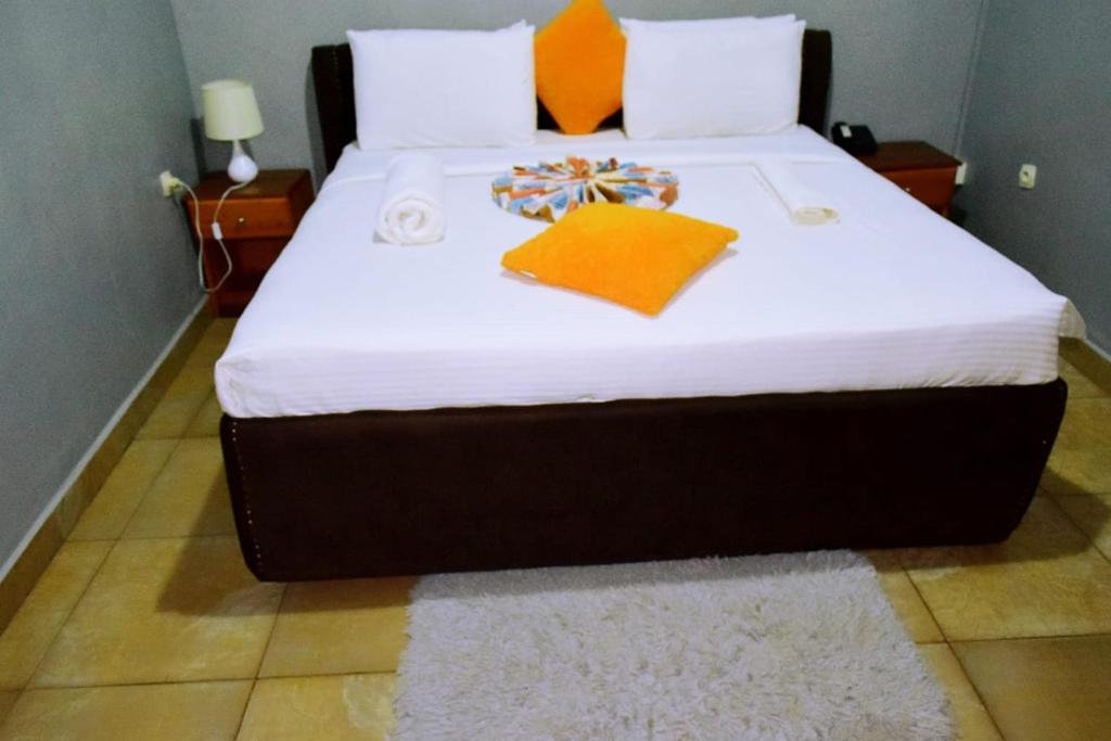 a bedroom with a large bed with white sheets and orange pillows at GARDEN INN by AIRPORT inn ltd in Kigali
