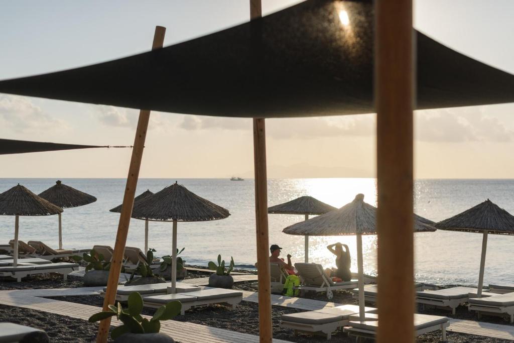 a beach with chairs and umbrellas and the ocean at Afroditi Venus Beach Resort in Kamari
