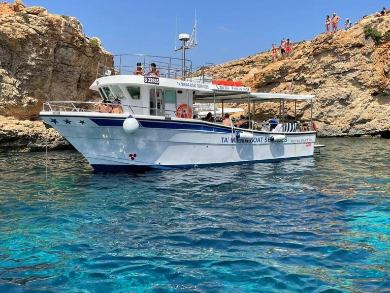 a white boat in the water next to a cliff at Comino Gozo Private Boat Trips Charters in Għajnsielem