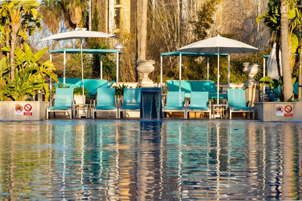 a pool of water with blue chairs and umbrellas at Bahía de Alcudia Hotel & Spa in Port d'Alcudia