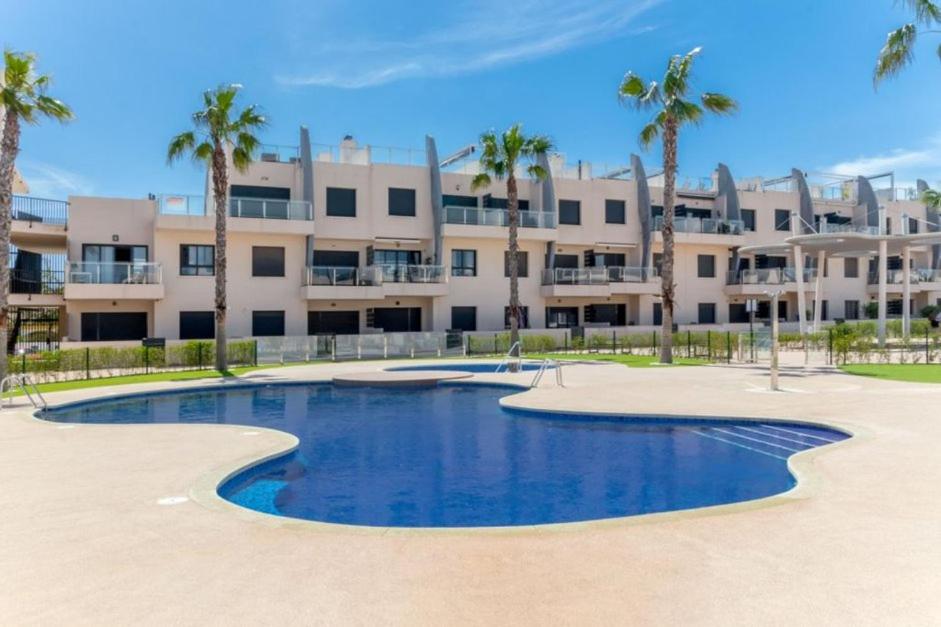 uma piscina em frente a um edifício com palmeiras em Bungalow cerca del mar em Torre de la Horadada