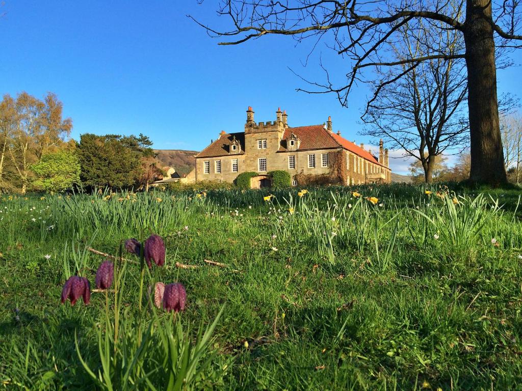 an old house in a field of grass with purple flowers at Finest Retreats - Ingleby Manor - Manor Cottage in Great Ayton