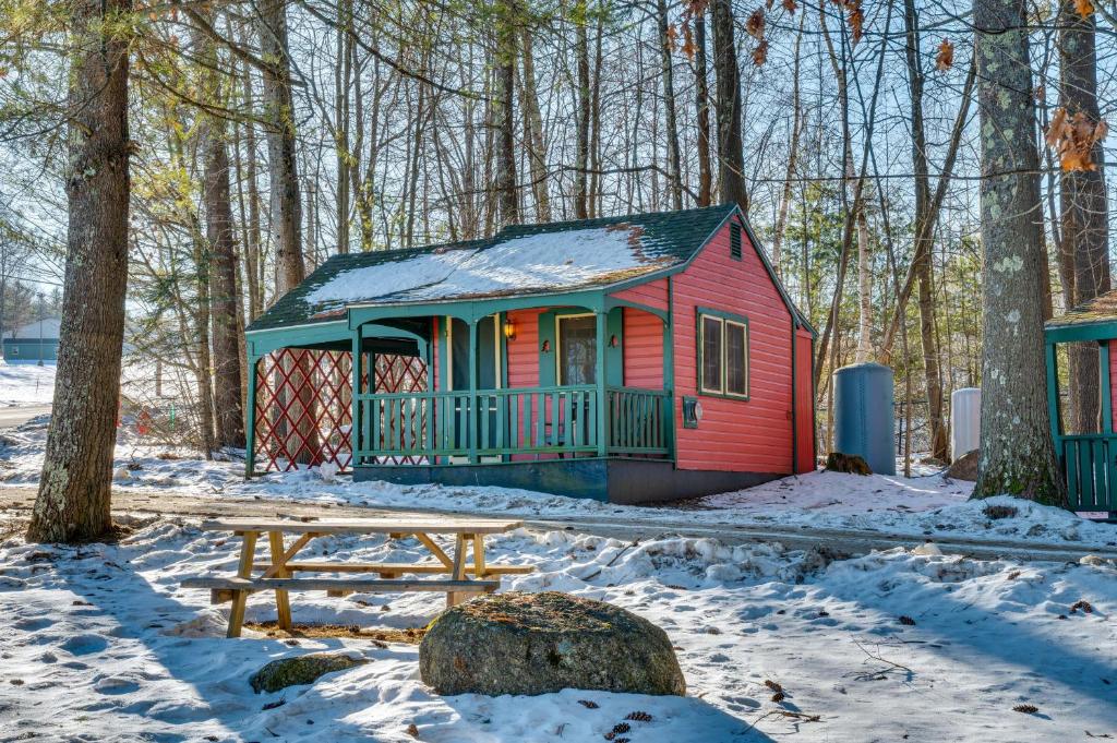 a small red house with a bench in the snow at Rustic Laconia Studio Cabin about 2 Mi to Weirs Beach! in Laconia