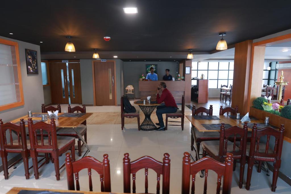 a restaurant with wooden tables and chairs and people in the background at Hotel Mangala Temple View in Guruvāyūr