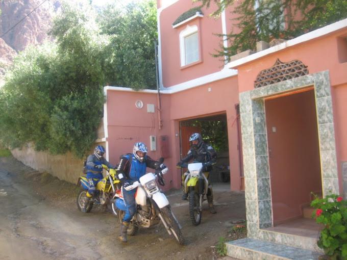 three people on motorcycles parked outside of a pink building at auberge djebel rose in Tafraoute