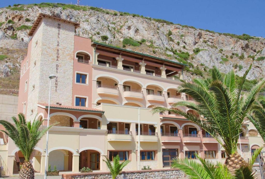 a building with palm trees in front of a mountain at Hotel La Rosa dei Venti in Buggerru