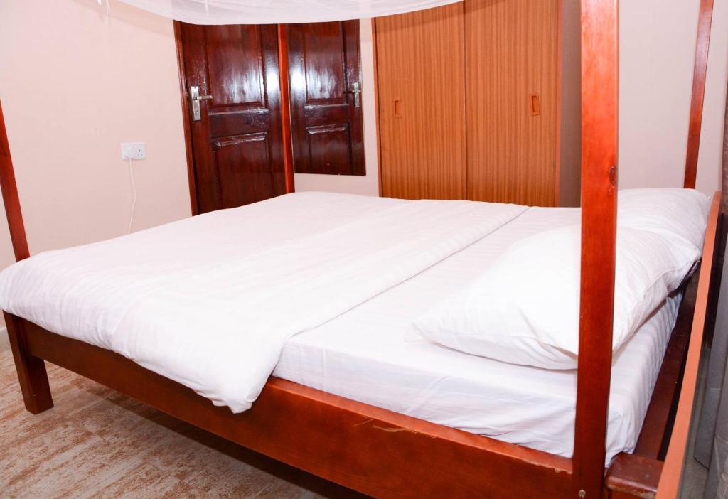 a bedroom with a bed with white sheets and wood at Safari Homes in Kampala