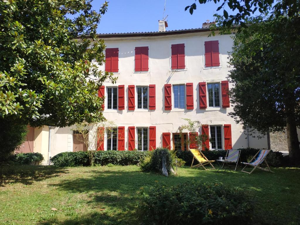 um edifício com persianas vermelhas e cadeiras num quintal em L'Arénoulat em Aspet