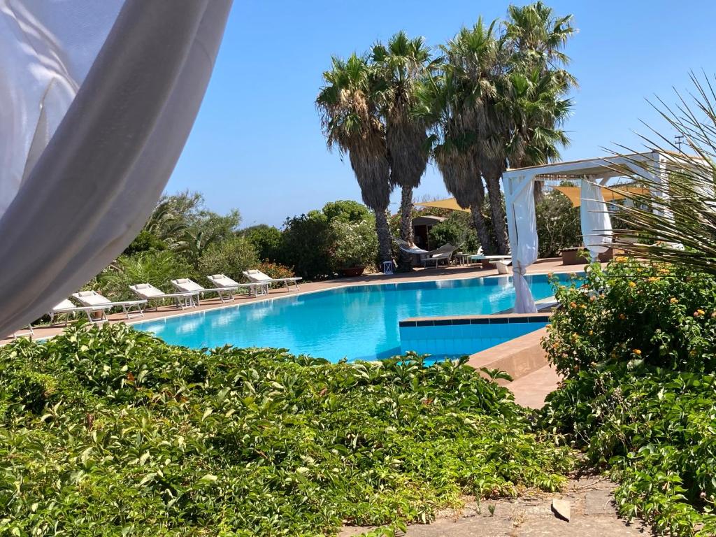 a large swimming pool with chairs and palm trees at Le Lanterne Resort in Pantelleria