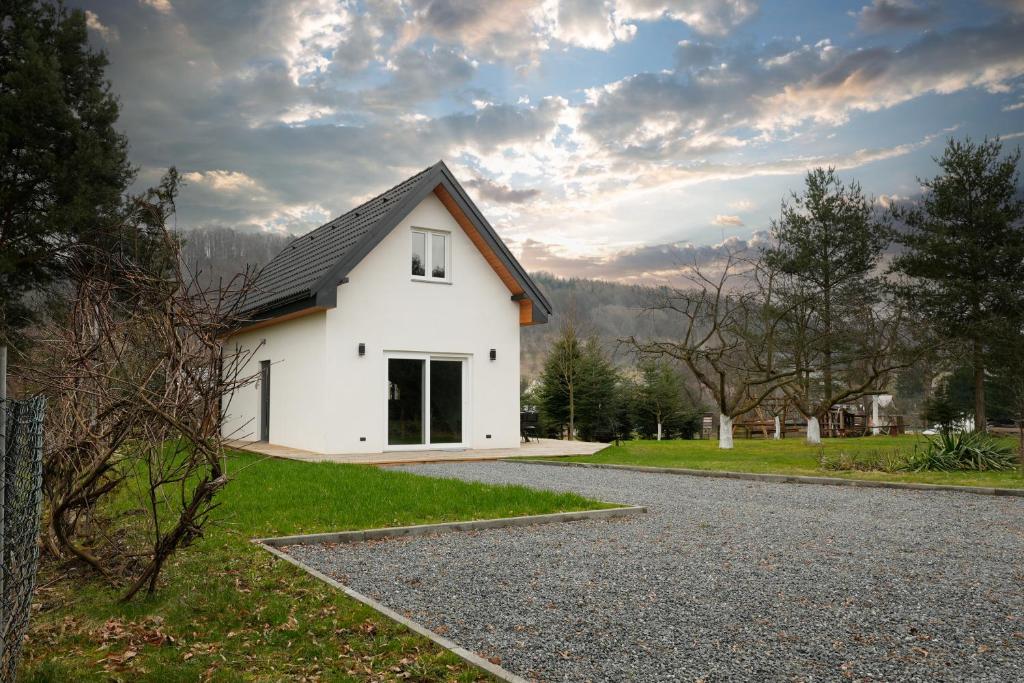 a white house with a black roof on a gravel road at Domki Kamea in Kudowa-Zdrój