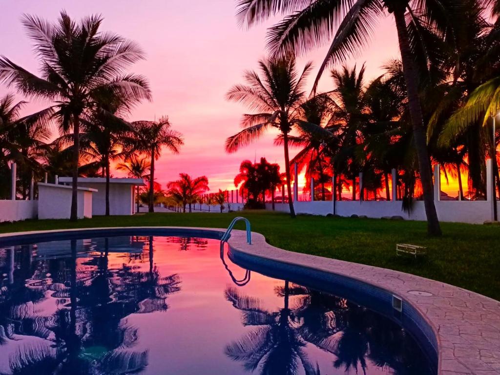 einen Pool mit Palmen und Sonnenuntergang in der Unterkunft Sunset in El Desengaño