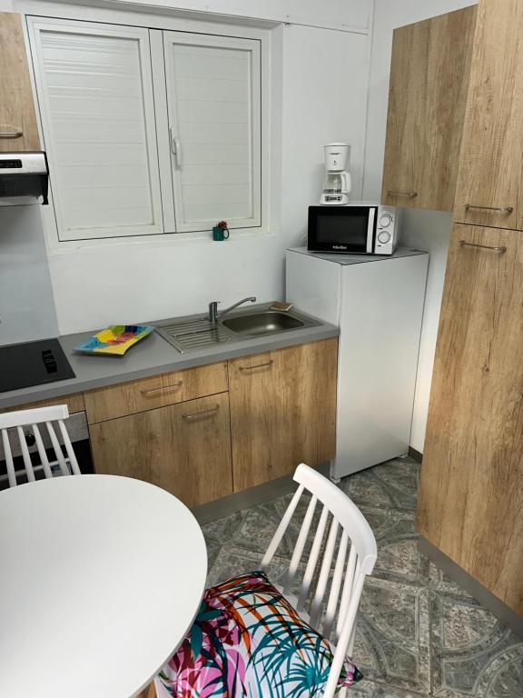 cocina con 2 sillas blancas y lavamanos en LE NID d'oiseau studio meublé climatisé chez l'habitant, en Deshaies