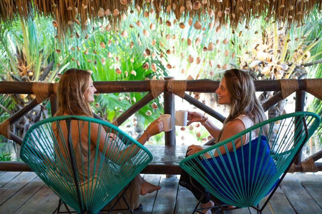 deux femmes assises à une table avec une tasse de café dans l'établissement Sirenas Caribbean Rooms Holbox, à Holbox