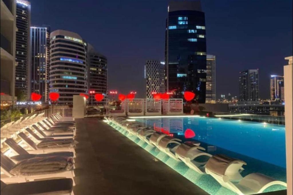 a pool with chairs and a city skyline at night at Modern Apartment close to Burj Khalifa in Al Faq‘