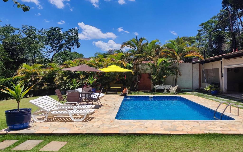 a swimming pool in a yard with chairs and an umbrella at Chácara Flores de Maio in Atibaia
