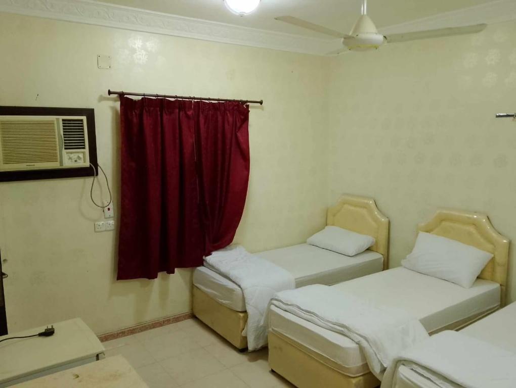 a room with two beds and a window with a red curtain at عمارة سكنية مخدومة قريبه من الحرم in Al Khansāk