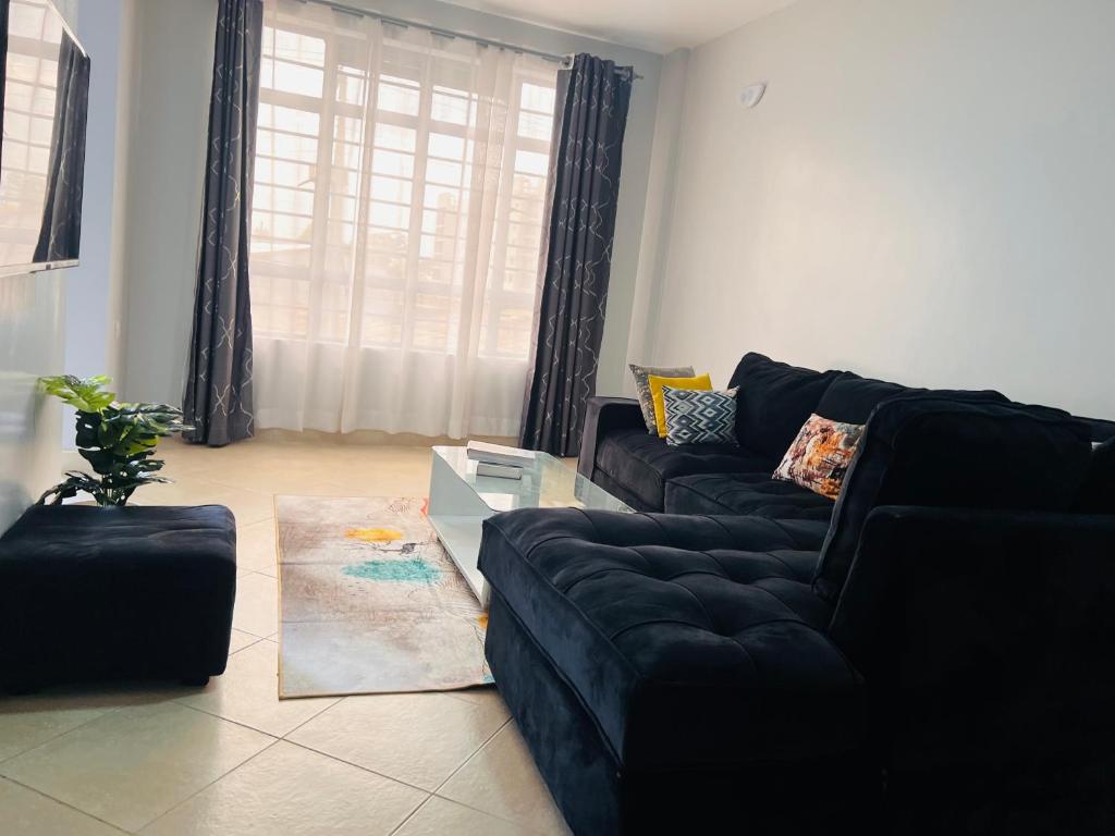 a living room with a black couch and a window at Adjana’s Cozy apartment in Nairobi