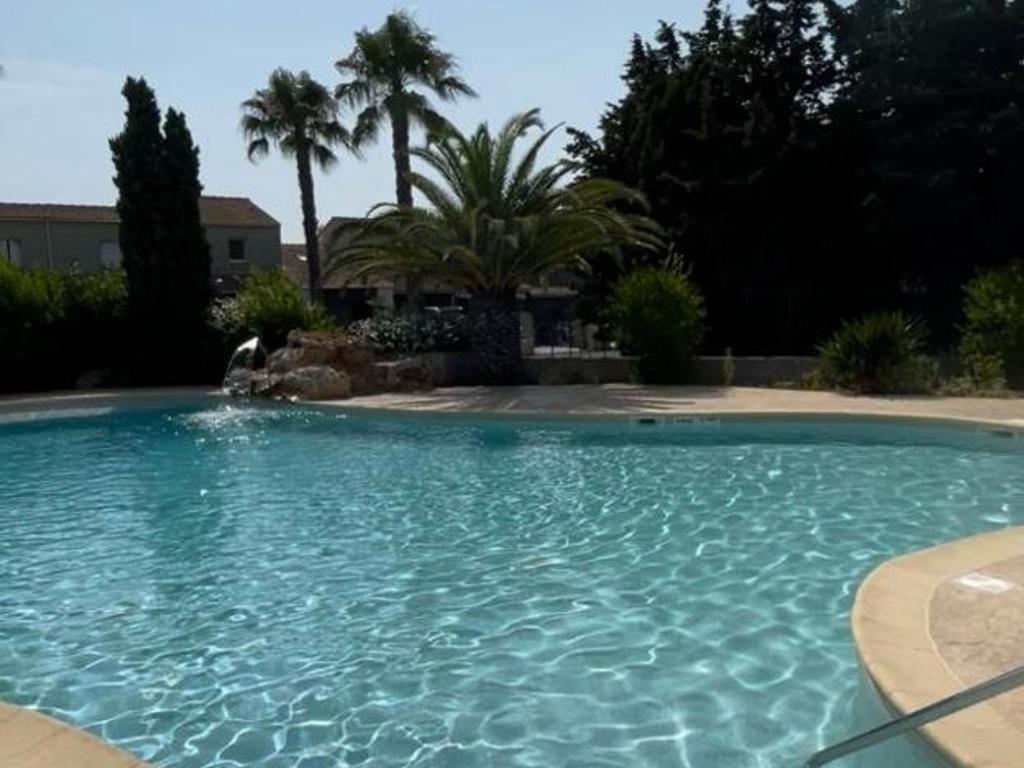 een groot blauw zwembad in een tuin met palmbomen bij Appartement Valras-Plage, 3 pièces, 4 personnes - FR-1-701-78 in Valras-Plage