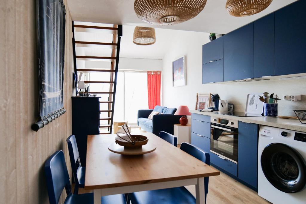 een keuken en een woonkamer met een houten tafel en blauwe kasten bij Appartement rénové avec goût et idéalement situé à deux pas du remblai in Les Sables-dʼOlonne