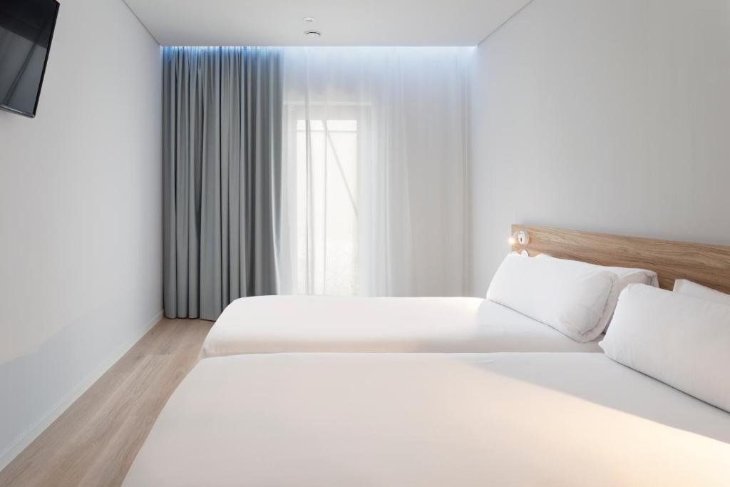 a white bedroom with two beds and a window at B&B HOTEL Olhão Algarve in Olhão